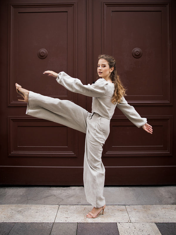 Girl raising leg and dancing on the street in natural linen pants and shirt