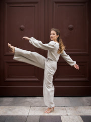 Girl raising leg and dancing on the street in natural linen pants and shirt